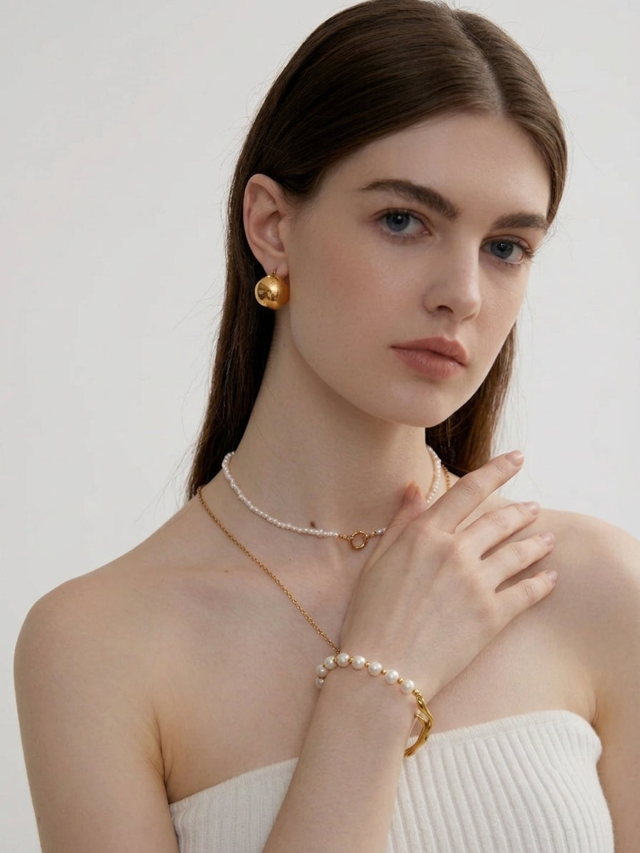 Woman wearing gold jewelry including earrings, necklace, and bracelet on a plain background