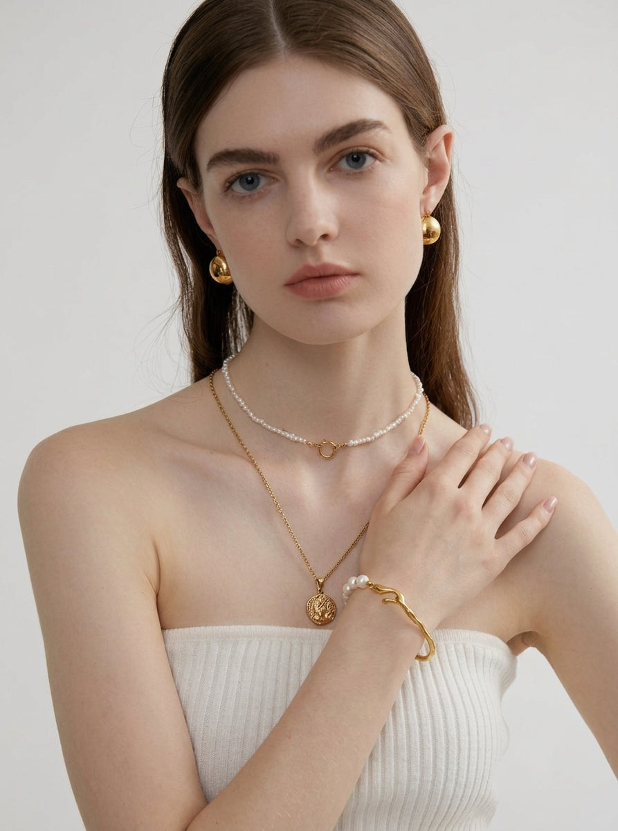 Woman wearing gold jewelry including a necklace, bracelet, and earrings on a plain background