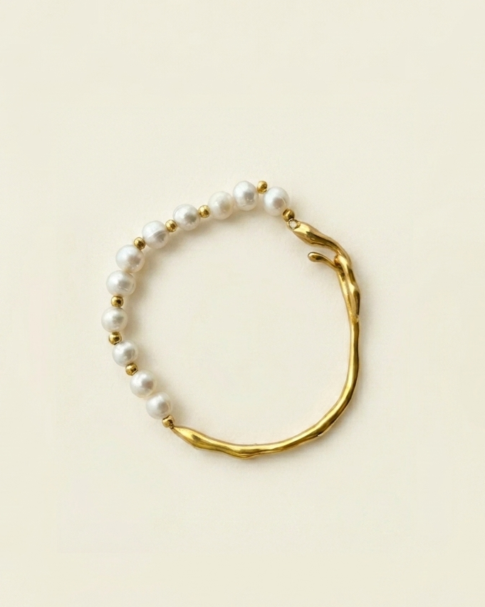 Gold bracelet with white beads on a beige background
