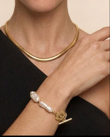 Woman wearing gold jewelry including earrings, necklace, and bracelet on a beige background