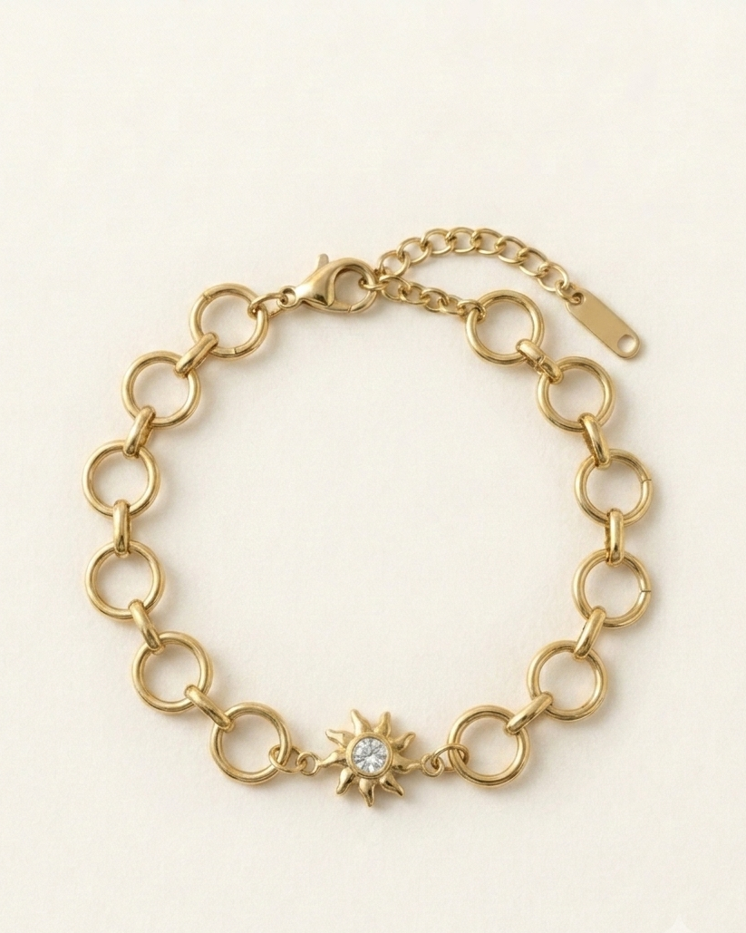 Gold chain bracelet with a sun-shaped charm on a light beige background