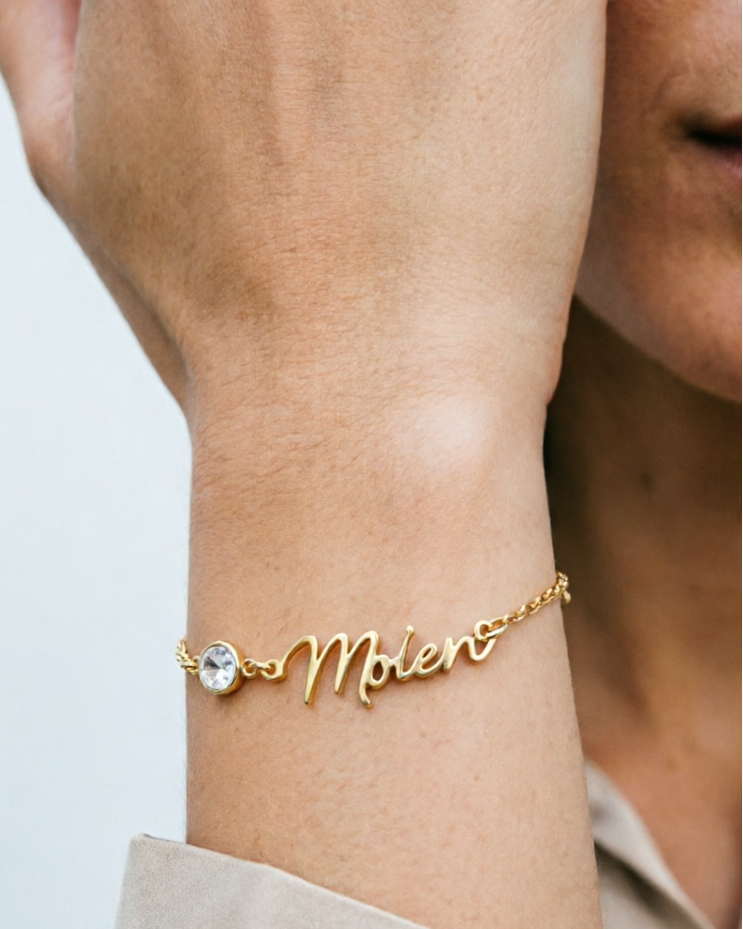 Gold bracelet with 'Molen' on a wrist against a neutral background