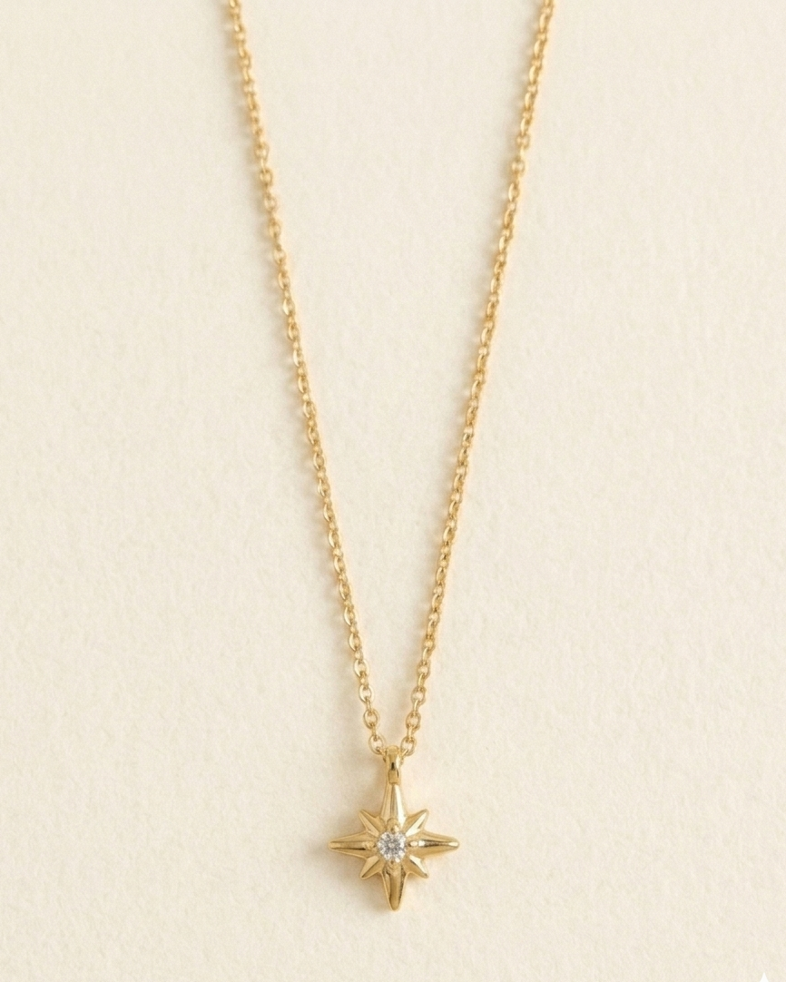 A delicate gold chain necklace with a small gold compass star pendant featuring a clear central gemstone