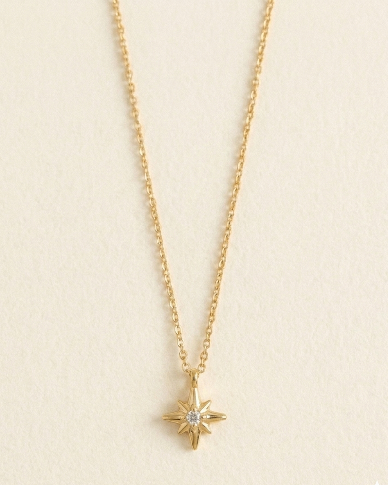 A delicate gold chain necklace with a small gold compass star pendant featuring a clear central gemstone