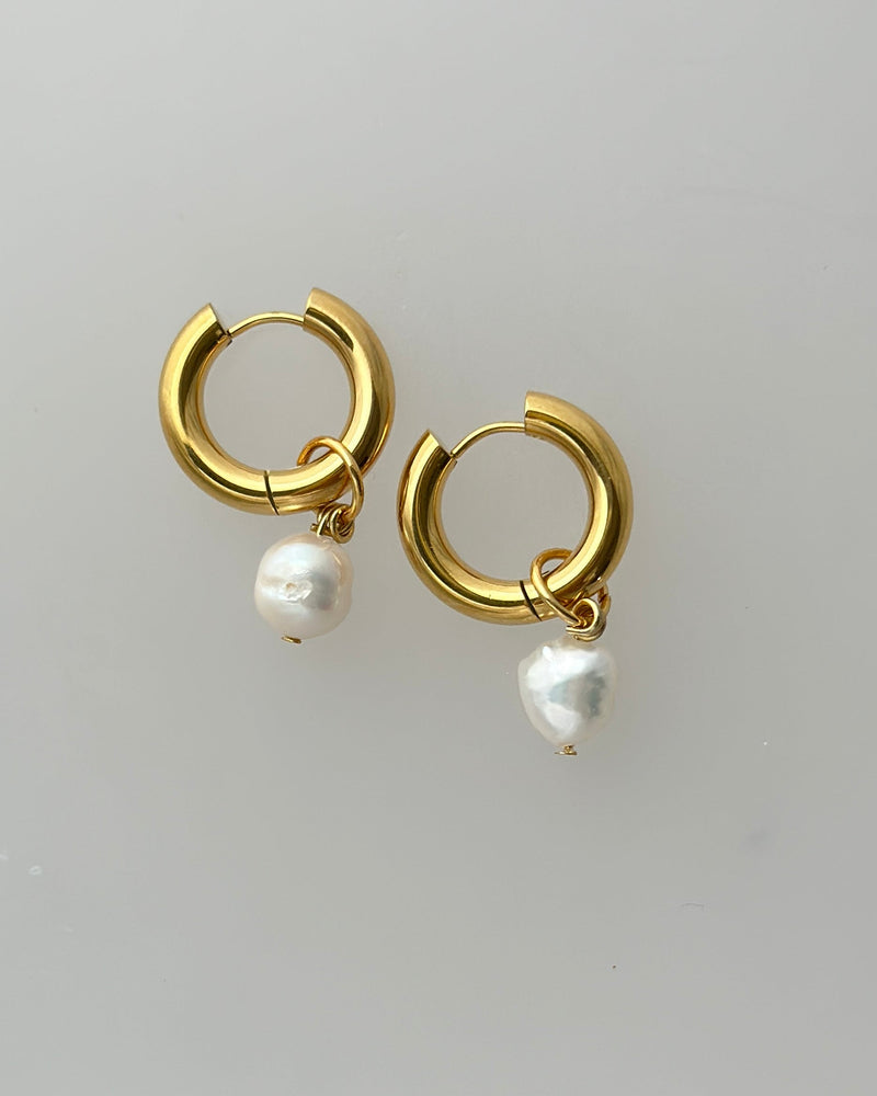 Gold hoop earrings with pearl drops on a light gray background